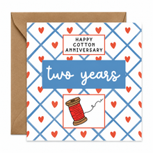 A square greeting card with a kraft envelope behind it. The card has a white background with a blue lattice pattern, small red hearts, and a central blue banner reading 'two years.