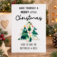 Plantable Christmas seed paper gift. The card reads 'HAVE YOURSELF A MERRY LITTLE Christmas SEEDS TO SAVE THE BUTTERFLIES & BEES!' and features a watercolor-style green Christmas tree made from wildflower seedpaper.