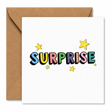 A square white greeting card with the word "SURPRISE" spelled out in colorful bubble letters and small yellow stars, shown with a brown kraft envelope behind it on a white background.