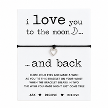 A black cord bracelet with a small silver heart charm displayed on a white card that reads 'i love you to the moon and back. Wish instructions included. 