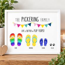 A framed personalised family flip-flop print. The white-framed artwork reads 'THE PICKERING FAMILY' and 'LIFE IS BETTER IN FLIP FLOPS!' with colourful illustrated flip-flops labeled with family members names, plus small paw prints.