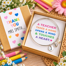 Personalised teacher charm bracelet with 3 charms. A silver bangle bracelet with a heart charm and initial pendant displayed in an open kraft gift box, displayed on a thank-you teacher card reading 'THANK YOU MRS SMITH. Teacher gift.