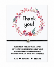 Thank you gift. A square white card with a watercolour floral wreath and the words 'Thank you!' above a black bracelet with a small silver star charm. Below the wish bracelet are the instructions.