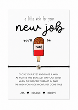 A white rectangular card with printed text and a popsicle illustration, tied with a black cord bracelet and a small star charm. The card reads, 'a little wish for your new job you'll be fab!' and includes additional blessing text below. Gift for new job.
