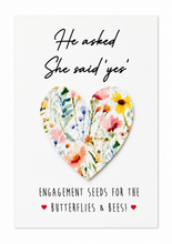 Wildflower Engagement seeds. A white greeting card with the text 'He asked She said yes' and 'Engagement seeds for the Butterflies & Bees!'  with a removable floral heart-shaped seed paper attached in the centre. Engagement gift.