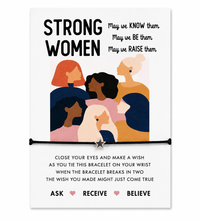 A square white card with the words “STRONG WOMEN” and an illustrated group of women, tied with a black bracelet across the lower middle. Smaller text appears on the card, and the bracelet includes a small star charm. Gift for international women’s day.