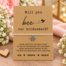 Bridesmaid proposal wish string bracelet. A kraft card with the text 'Will you bee our bridesmaid?' and a small bee charm tied with a white string. Bridesmaid gift 