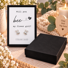 A pair of silver bee stud earrings displayed on a white card inside a black presentation box. The card reads 'Will you bee my flower girl? STERLING SILVER'.