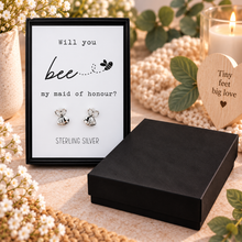 A pair of silver bee stud earrings displayed in a black presentation box with a printed card that reads 'Will you bee my maid of honour?'.