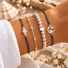 Set of four delicate bracelets: two grey cord bracelets, one silver chain bracelet, and one silver beaded bracelet with a heart charm and a circular map charm. 4 cord and silver bracelet set 