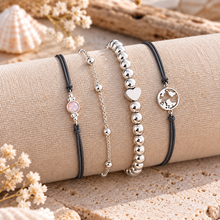 Set of four delicate bracelets: two grey cord bracelets, one silver chain bracelet, and one silver beaded bracelet with a heart charm and a circular map charm. 4 cord and silver bracelet set 