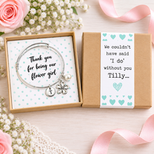 Personalised Thank you for being our flower girl charm bangle. A silver charm bracelet presented in a green polka dot gift box. The bracelet has a round silver bracelet with a flower charm, a small pearl bead, and a round initial charm. Flower girl gift.