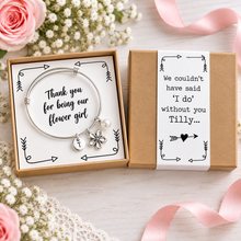 Personalised Thank you for being our flower girl charm bangle. A silver charm bracelet presented in a black and white gift box. The bracelet has a round silver bracelet with a flower charm, a small pearl bead, and a round initial charm. Flower girl gift.
