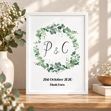 A personalised print with a green eucalyptus wreath and the initials and wedding date and location 
