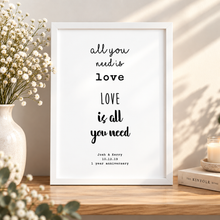 A white framed typographic art print with black text reading 'all you need is love LOVE is all you need' and personalised anniversary. Personalised anniversary gift for paper anniversary 1 year