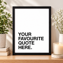 A black-framed typographic art print leaning on a wooden surface, with the text 'YOUR FAVOURITE QUOTE HERE.' on a white background.